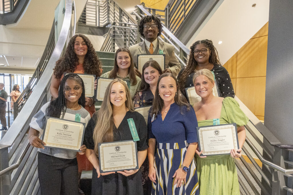 College of Health Professions Scholarship Ceremony, students pose in front of a staircase holding their scholarship certificates